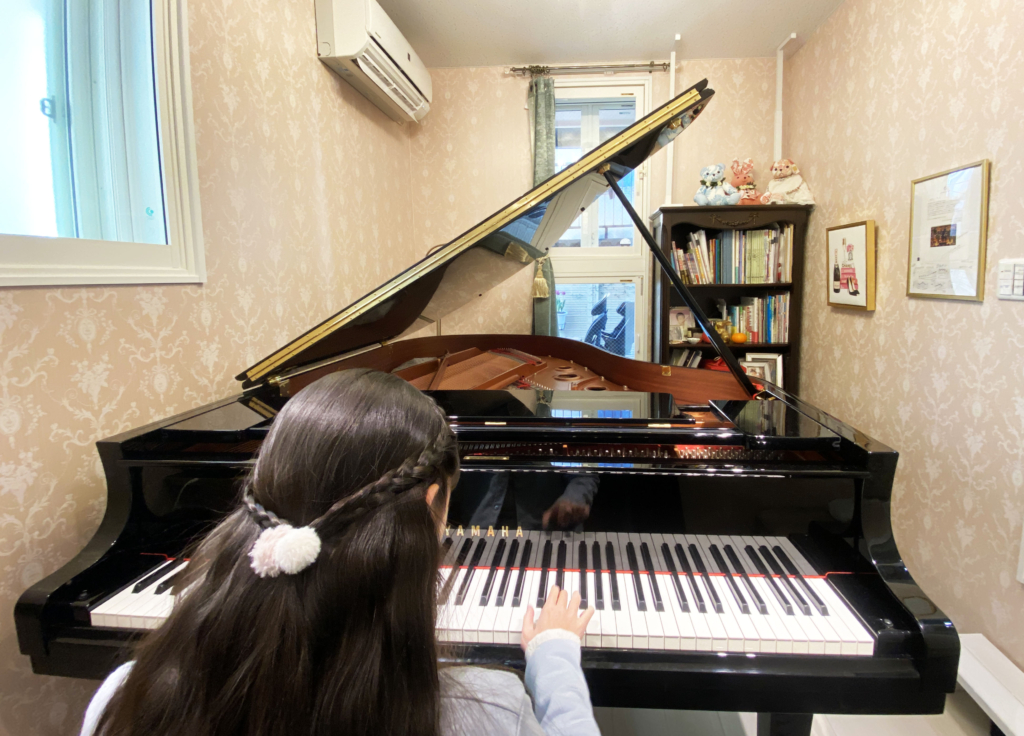 A child playing a grand piano inside a soundproof room.